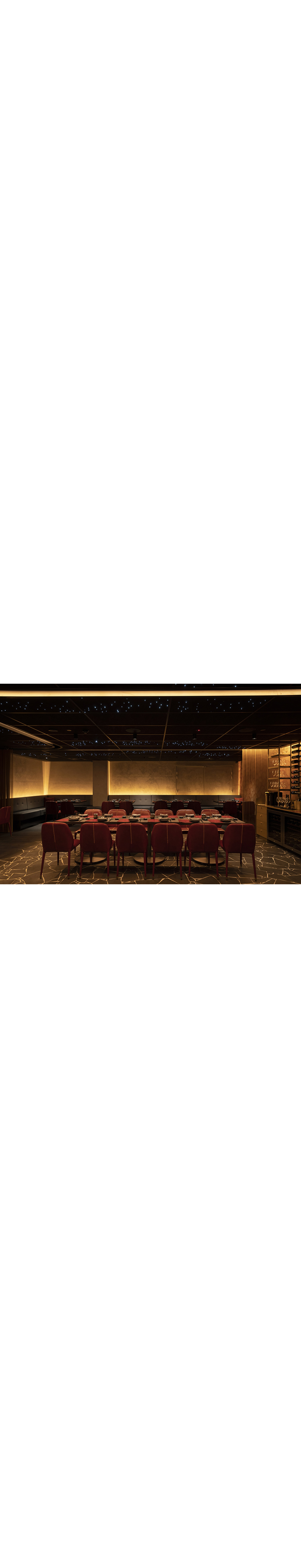 A dimly lit restaurant dining area with red chairs, dark tables, and a ceiling featuring small blue fiber optic lights.